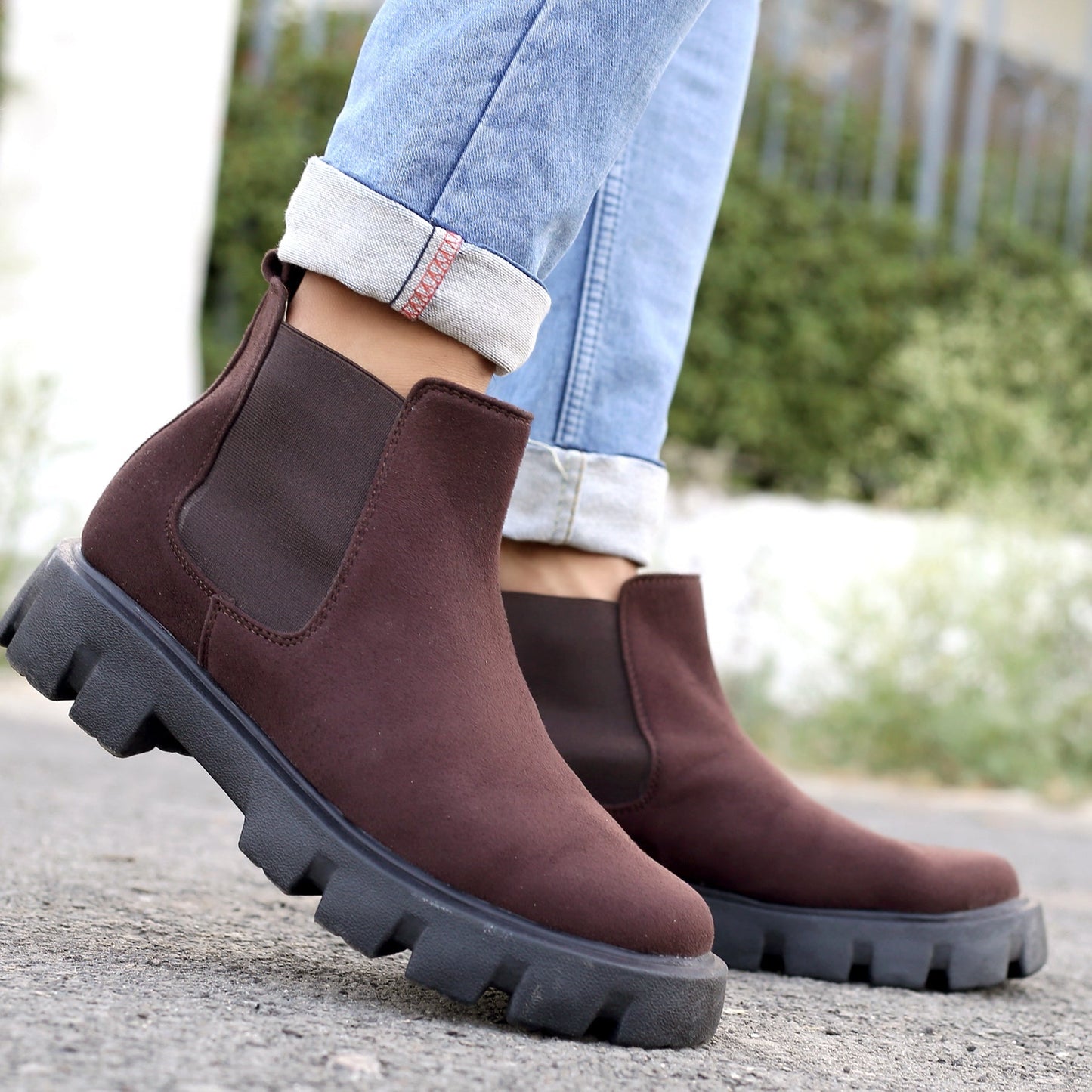 Brown Chelsea boots worn with rolled-up jeans on a blurred outdoor background