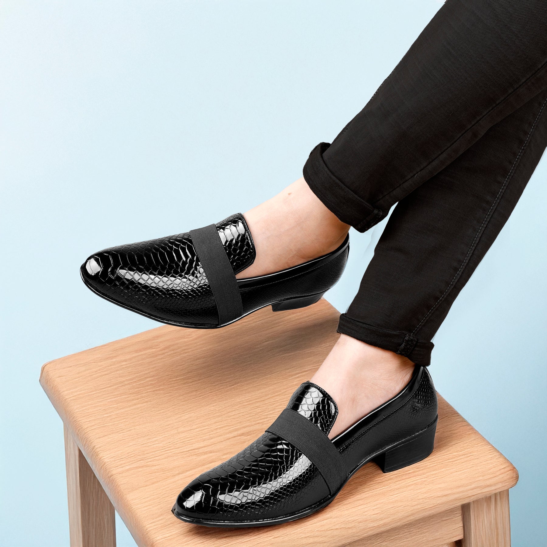 Black patent leather shoes worn by a person on a light blue background