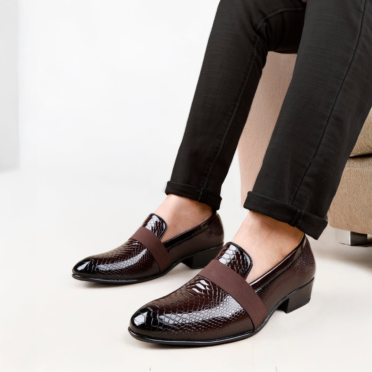 Brown dress shoes with snake print strap worn by a person sitting on a white background