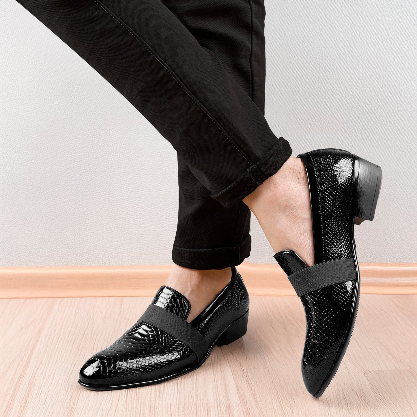 Black patent leather shoes worn with black pants on a light wooden floor.