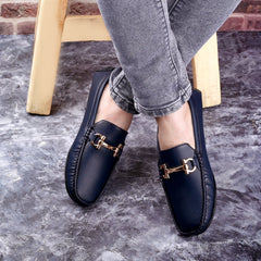 Person wearing navy loafers with gold buckles on a gray floor.
