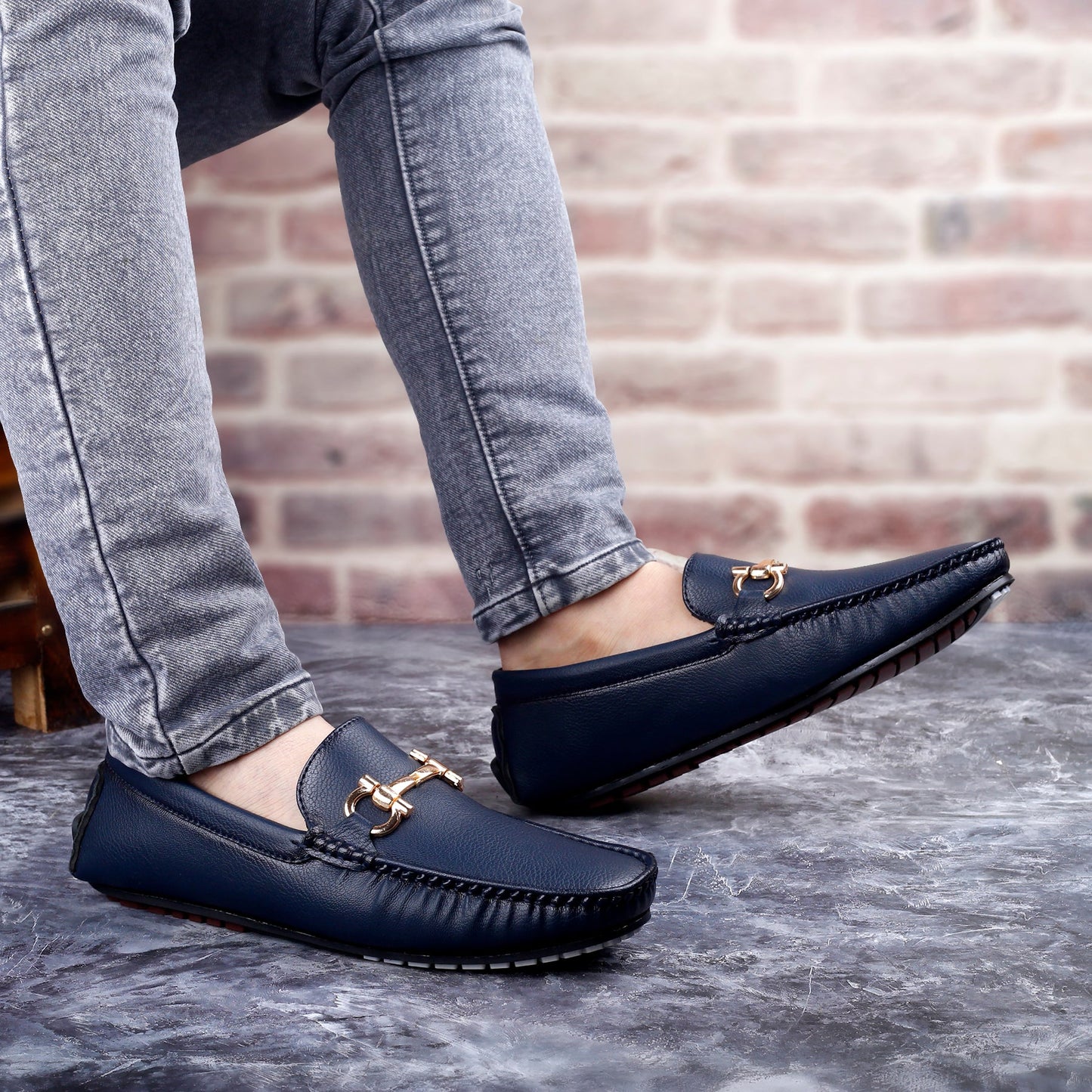 Navy loafers with gold accents worn by a person against a brick wall.