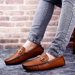 Brown loafers worn with gray jeans against a brick wall background