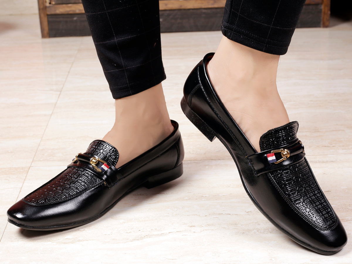Black dress shoes with decorative buckles worn by a person on a light wooden floor.