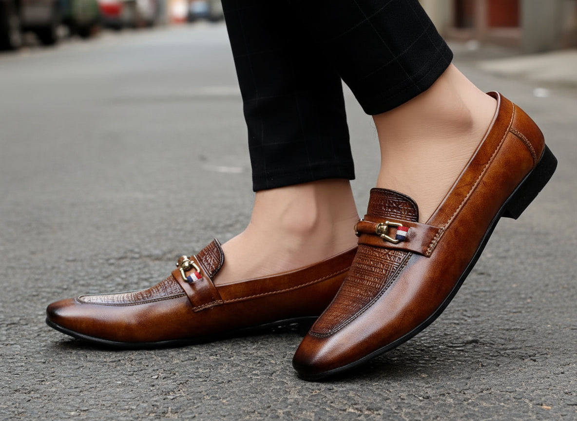 Brown leather loafers worn by a person on a light wooden floor.