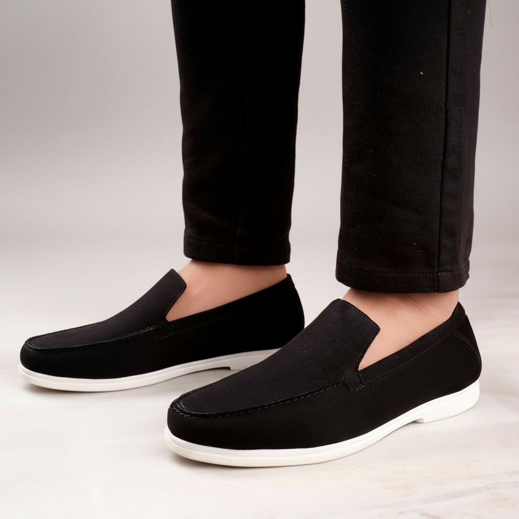 Black loafers worn with black pants on a light wooden floor.