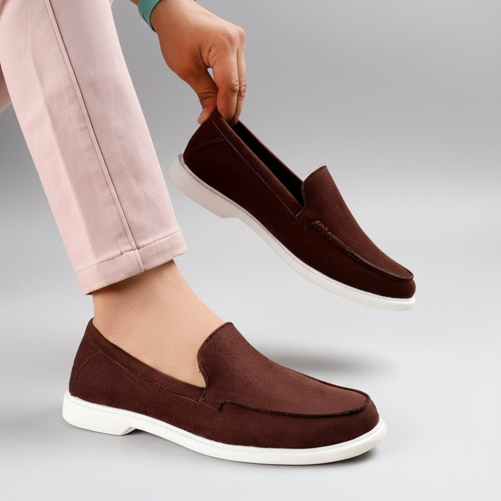 Brown loafers with white soles worn by a person, with one shoe being taken off.