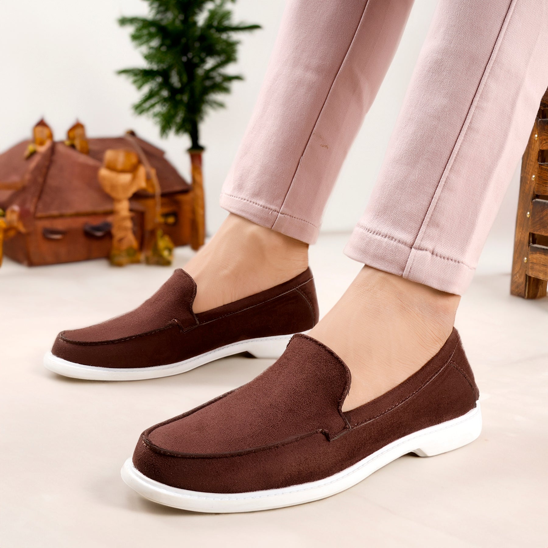 Brown loafers with white soles worn by a person, with a blurred indoor background.