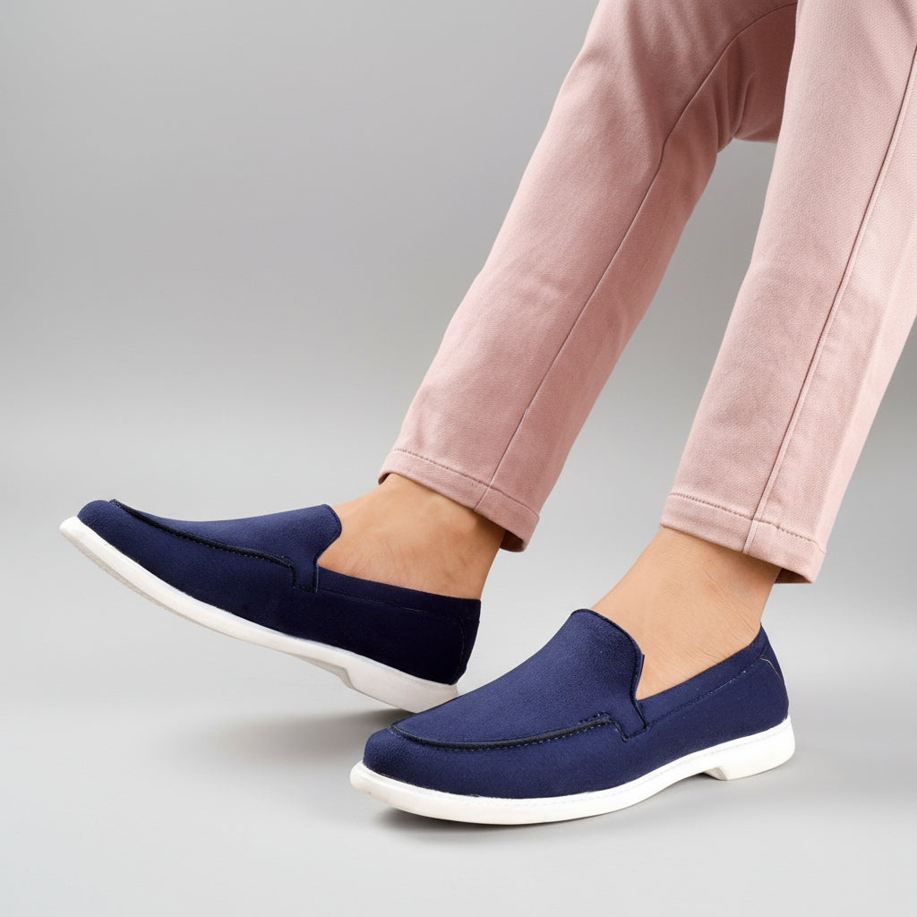 Navy loafers worn with pink pants on a light wooden floor.