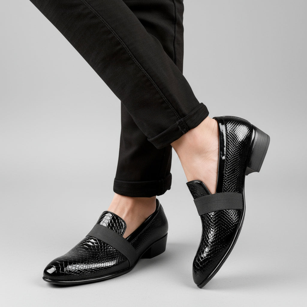 Black patent leather shoes worn with black pants on a light wooden floor.