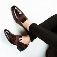 Brown patent leather shoes with a strap worn by a person on a white background