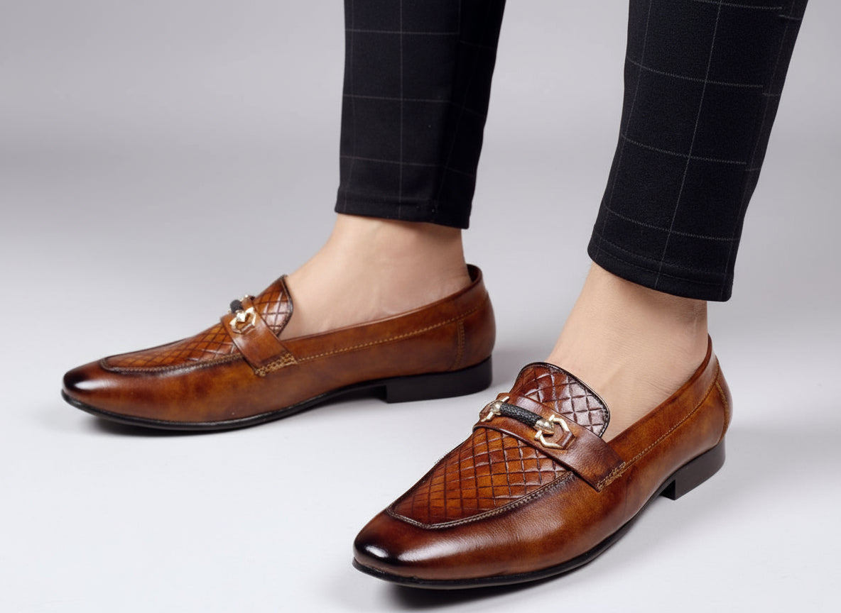 Brown leather loafers worn with checkered pants on a light wooden floor.