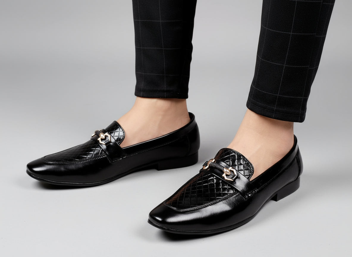 Black dress shoes with quilted design worn by a person on a light wooden floor.