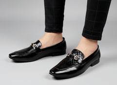 Black dress shoes with quilted design worn by a person on a light wooden floor.