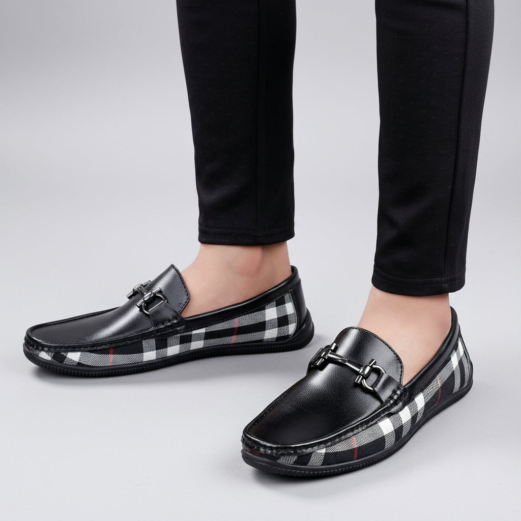 Black loafers with plaid pattern worn by a person on a wooden floor.