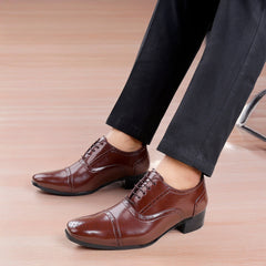 Brown dress shoes worn with black pants on a wooden floor.