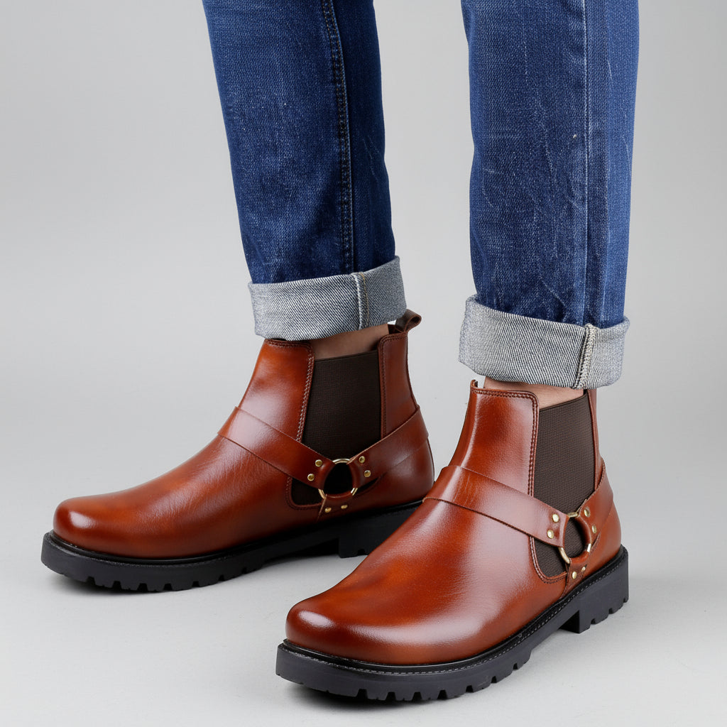 Brown leather boots with black soles worn with blue jeans on a wooden floor.