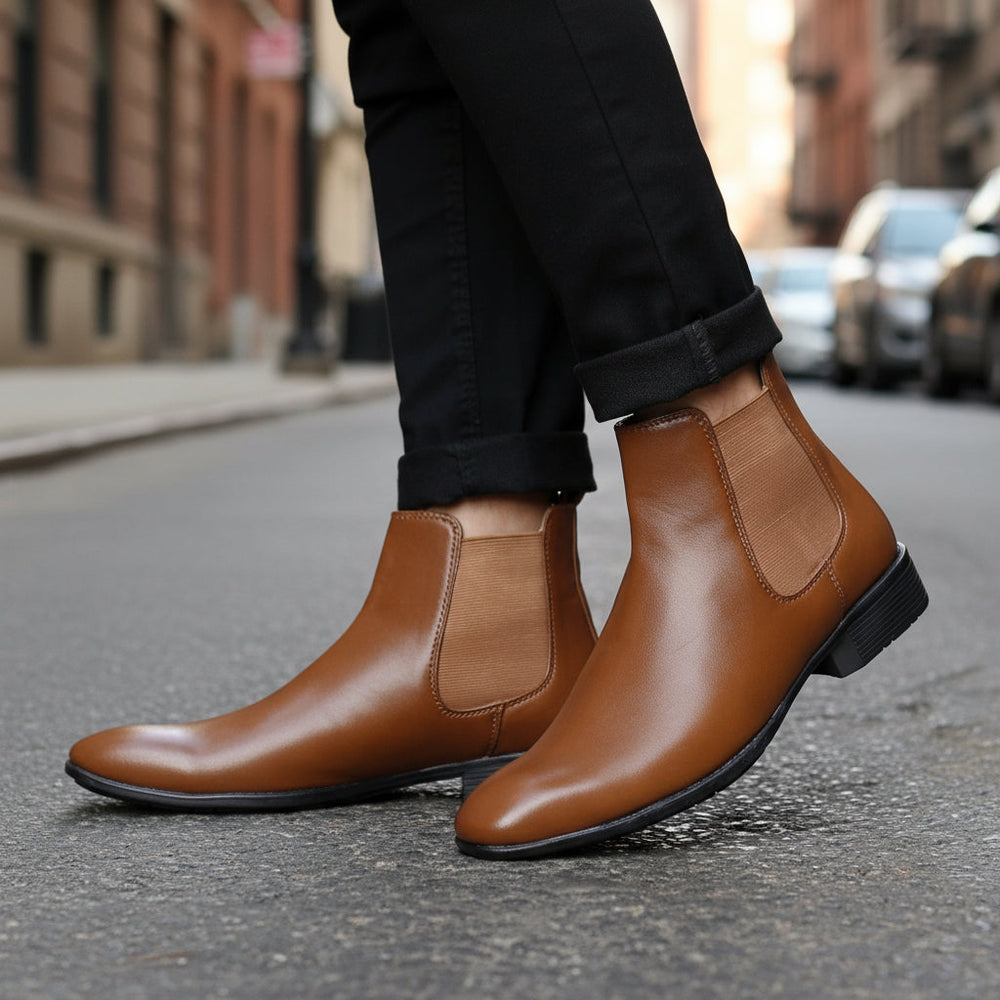 Brown leather Chelsea boots worn with black pants on a light background
