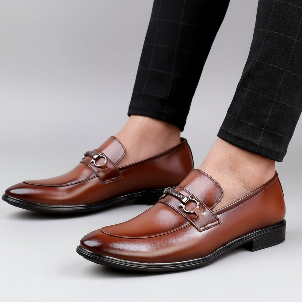 Brown leather loafers worn with black pants on a wooden floor.