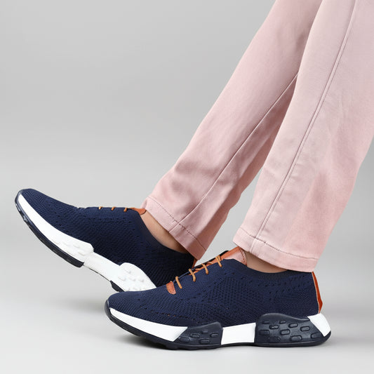 Navy blue athletic shoes with orange accents worn by a person on a wooden floor.