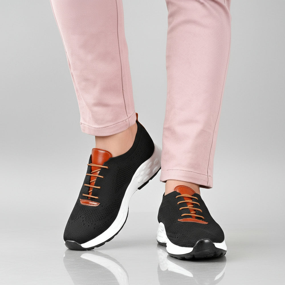 Black sneakers with white soles worn with pink pants on a wooden floor.