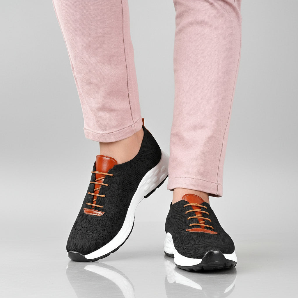 Black sneakers with white soles worn with pink pants on a wooden floor.