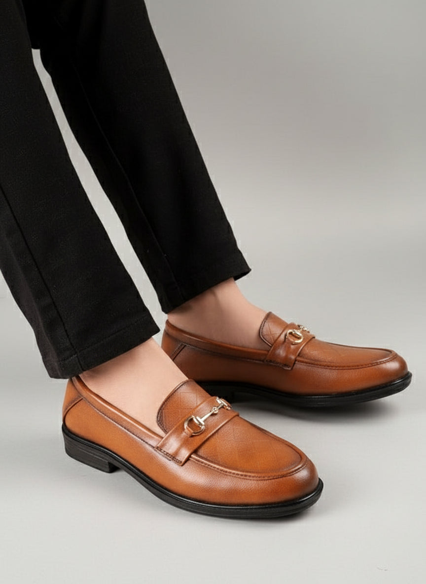 Brown leather loafers worn with black pants on a light wooden floor.