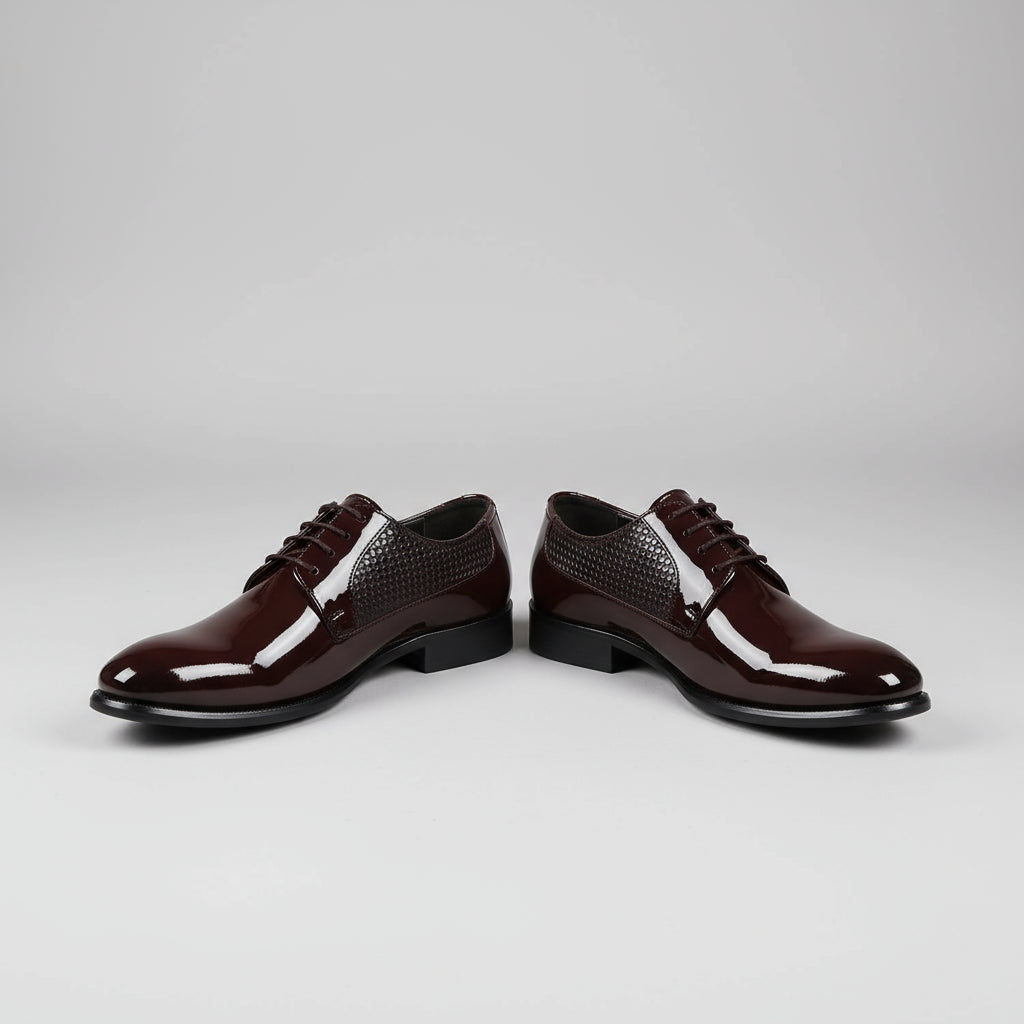 Person wearing shiny brown dress shoes with a blurred office setting in the background