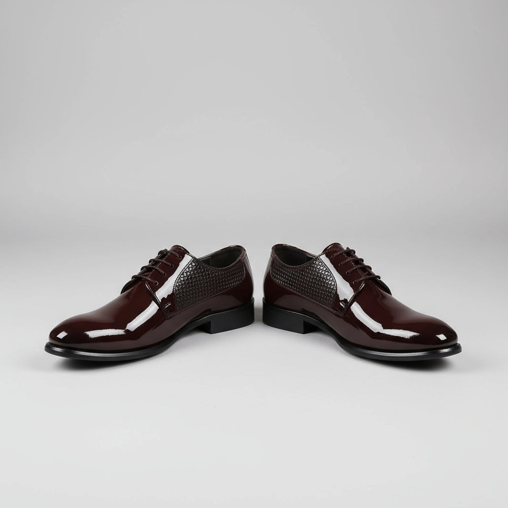 Person wearing shiny brown dress shoes with a blurred office setting in the background