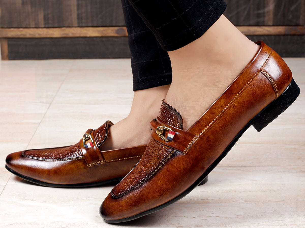 Brown leather loafers worn by a person on a light wooden floor.