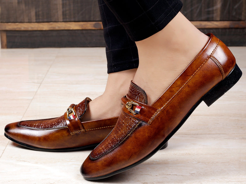 Brown leather loafers worn by a person on a light wooden floor.