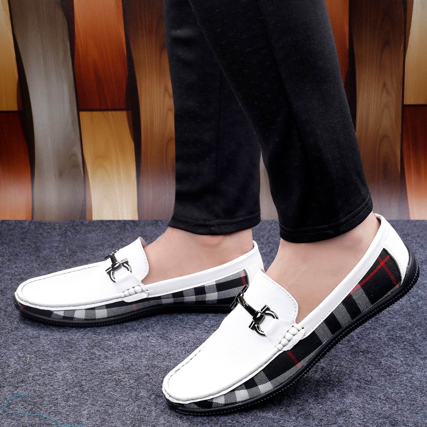 White loafers with black and red checkered soles worn by a person on a wooden floor.