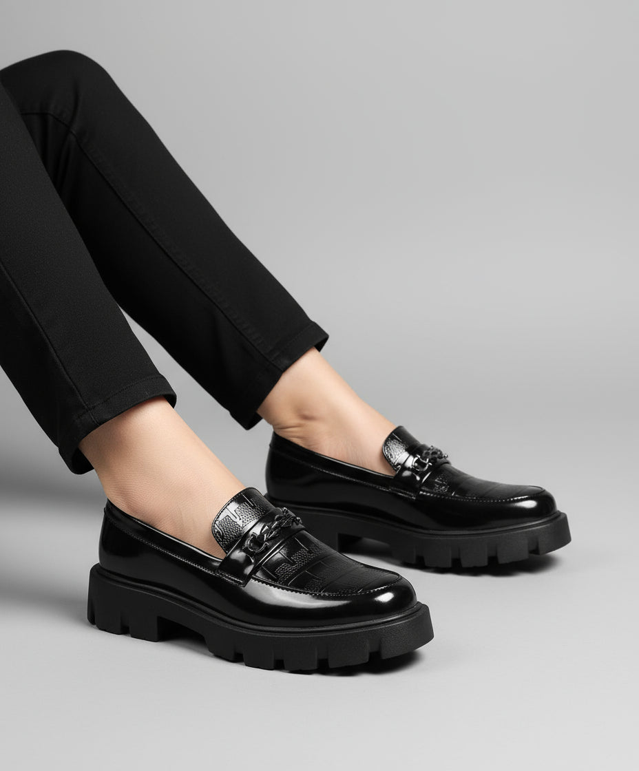 Person wearing black leather shoes on a textured gray surface with a white wall background