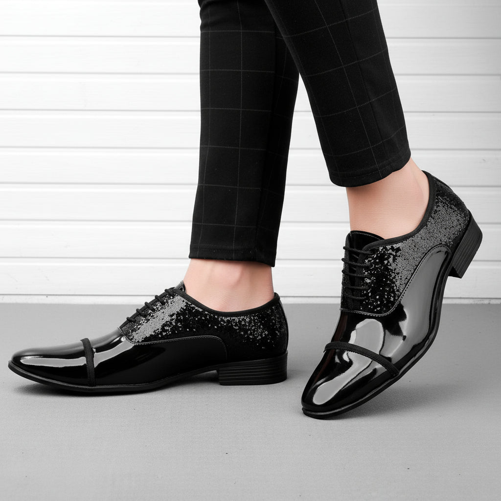 Black shiny dress shoes worn with black pants on a neutral background