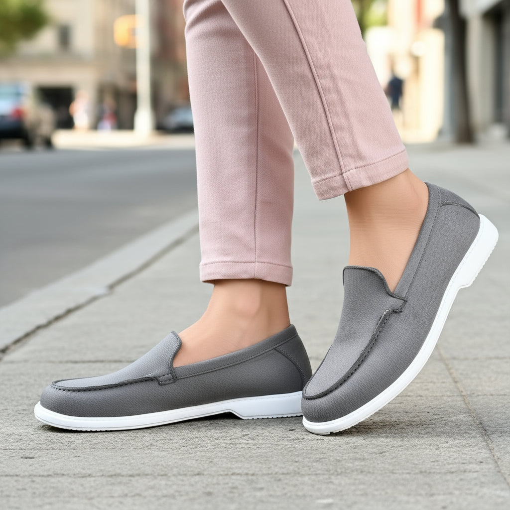 Person wearing gray loafers with white soles on a wooden floor.
