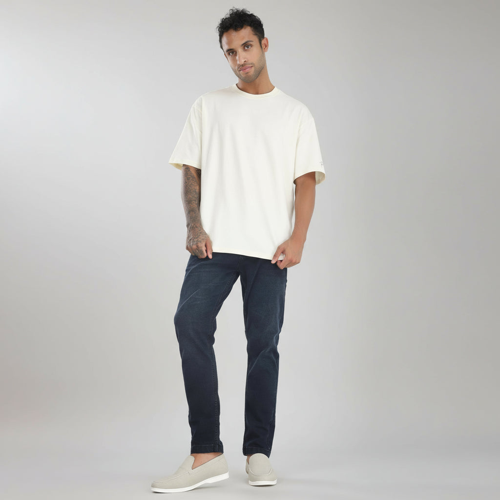 Man wearing a white t-shirt and dark jeans standing against a plain white background