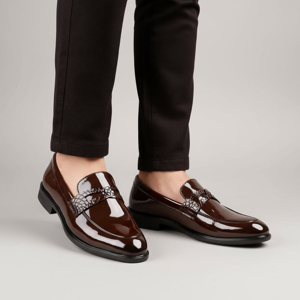Brown patent leather loafers worn with black pants on a neutral background